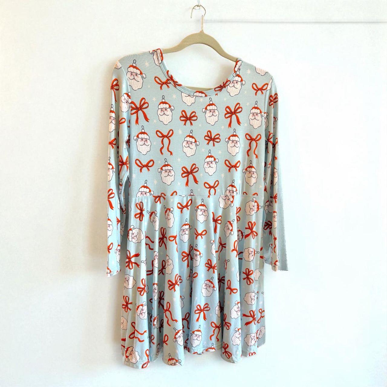 Long-sleeve dress with Santa Claus and bow pattern on a hanger against a white background