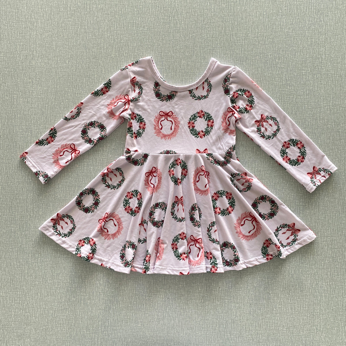 Pink dress with festive wreath and bow pattern on a light sand background