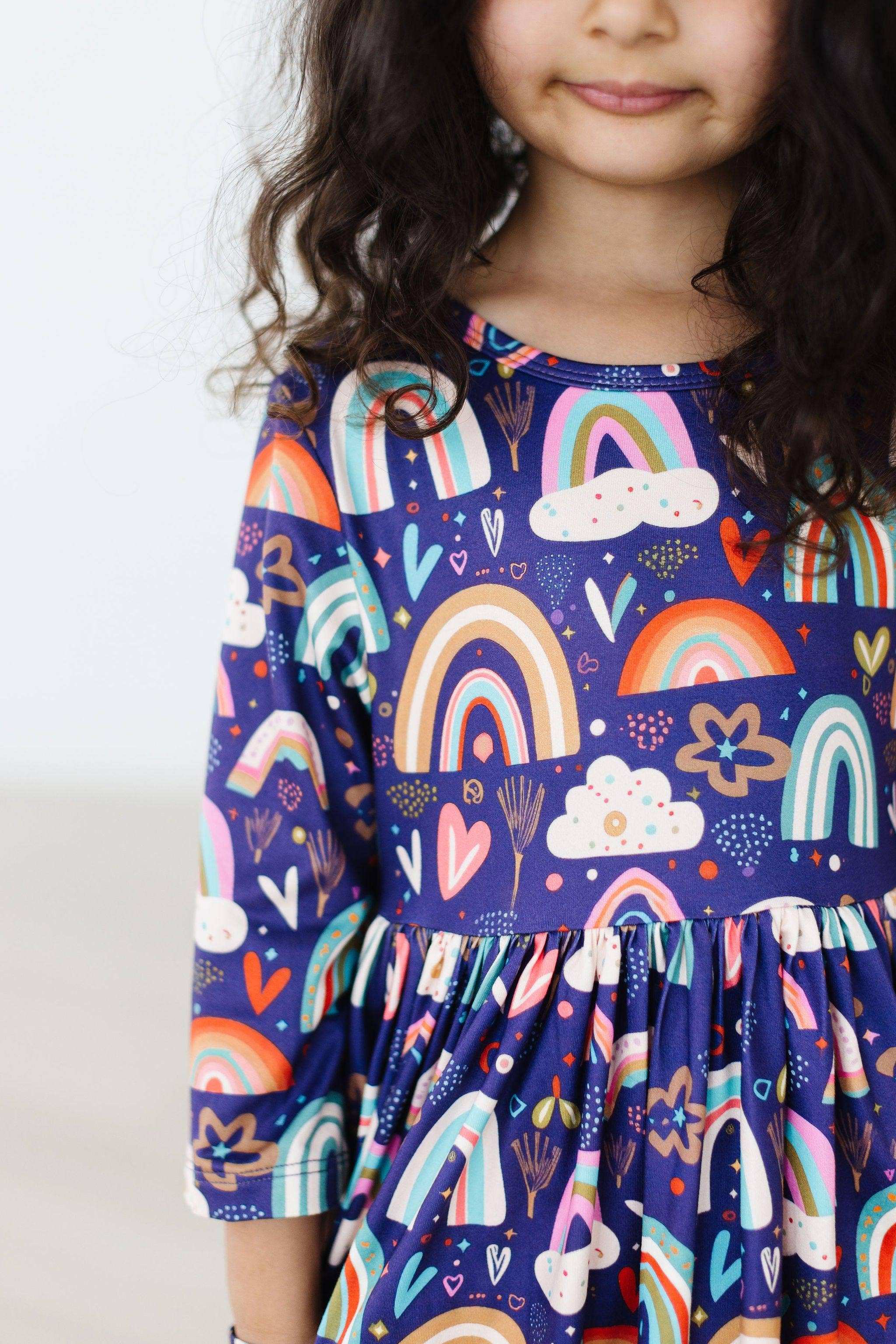 Child wearing a dress with colorful rainbow and cloud patterns on a white background