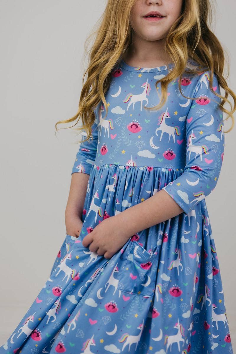 Young girl wearing a blue dress with unicorn pattern against a plain background