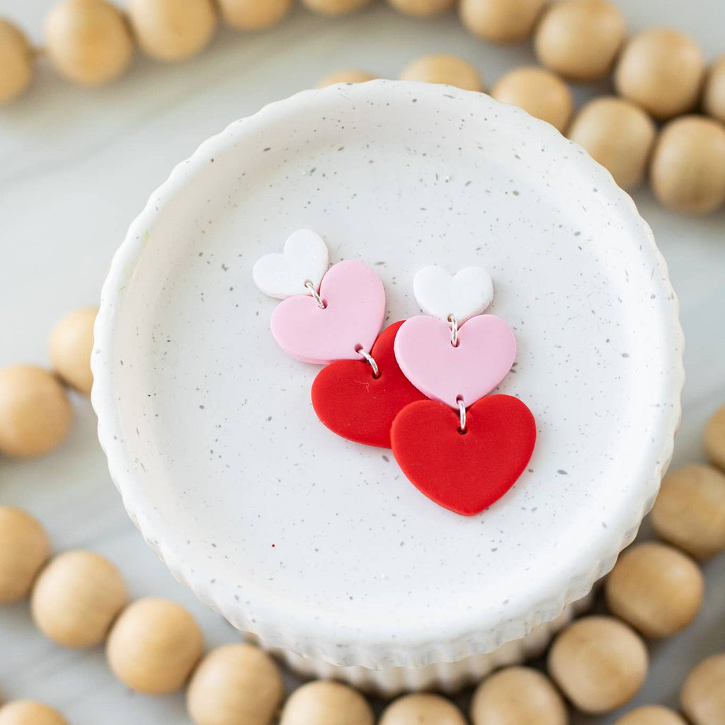 Heart-shaped earrings on a white dish with wooden beads around