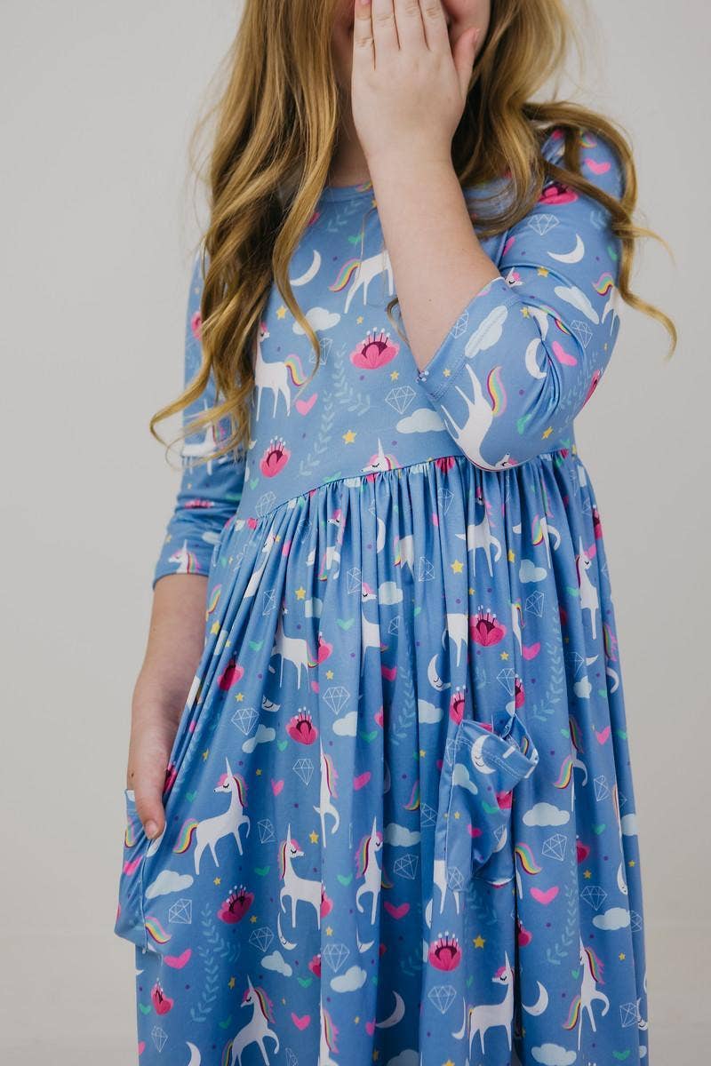Child wearing a blue dress with unicorn pattern on a plain background
