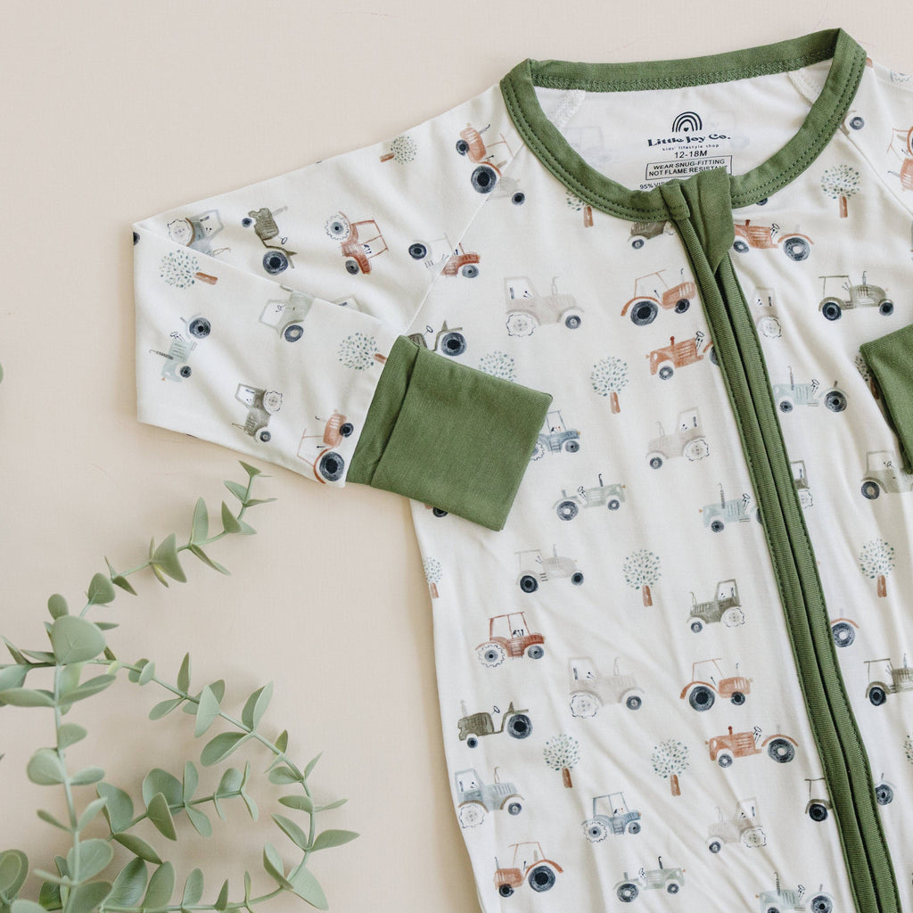 Baby outfit with green trim and tractor pattern on a beige background