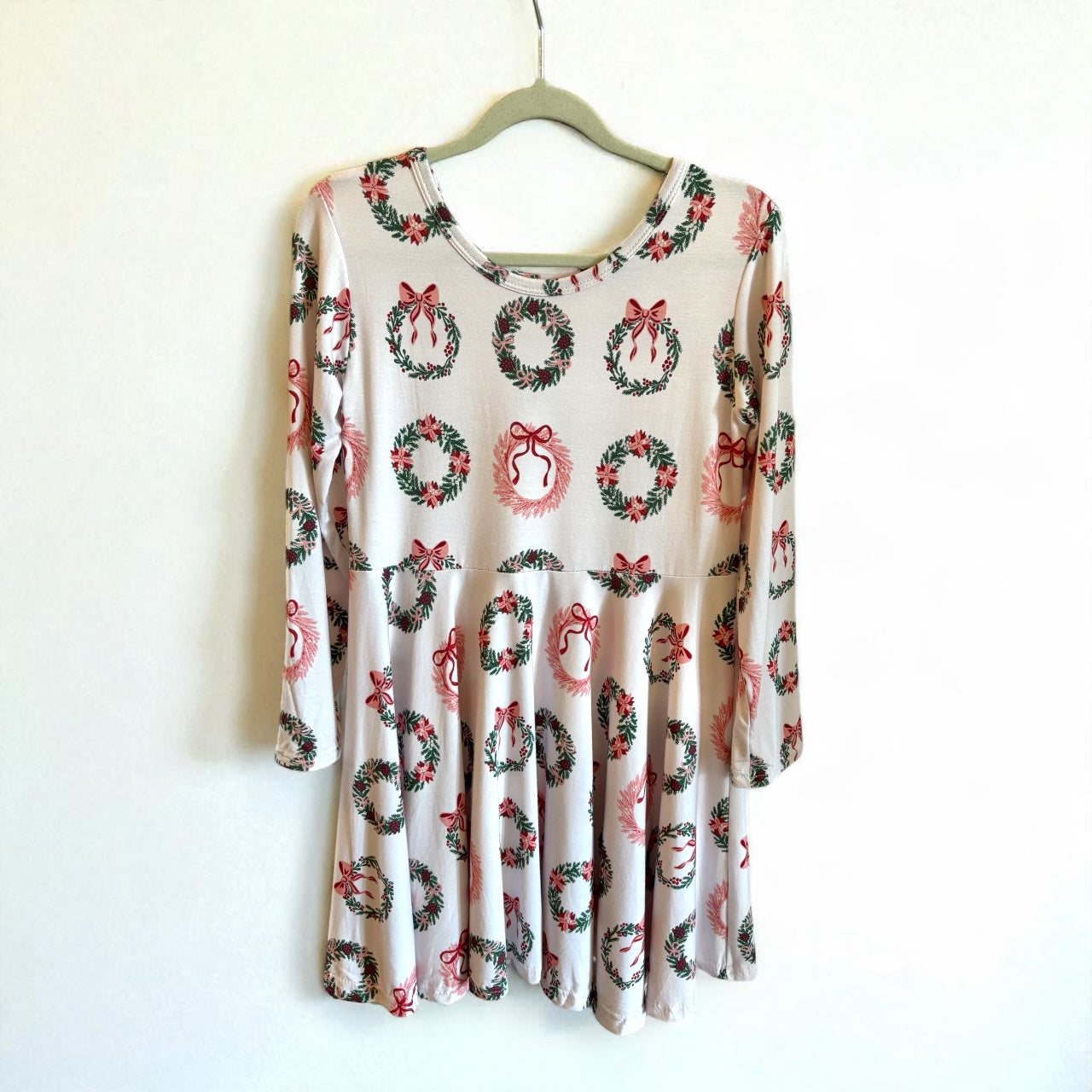 Long-sleeve dress with wreath and bow pattern on a hanger against a white background