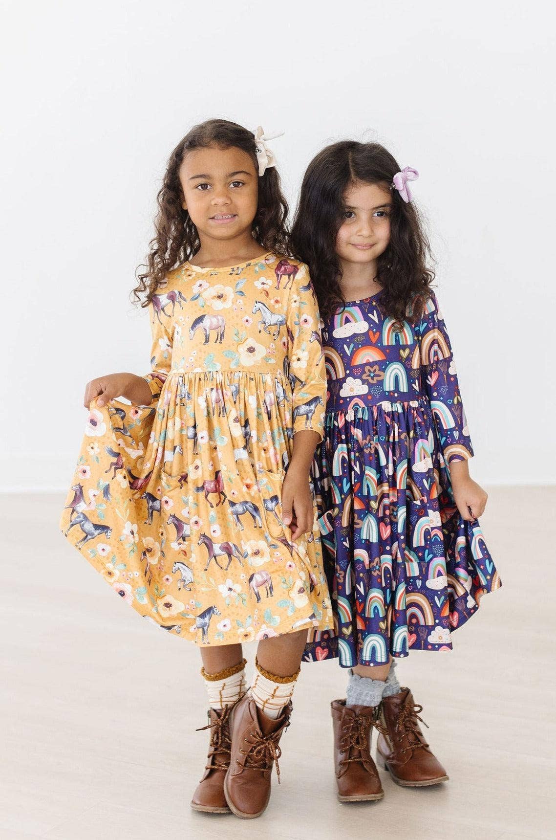 Two young girls wearing patterned dresses standing side by side on a white background