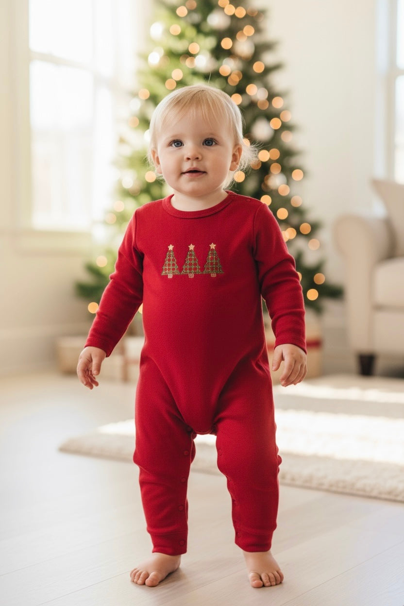 Child wearing a red Christmas-themed onesie in a room with a decorated tree.